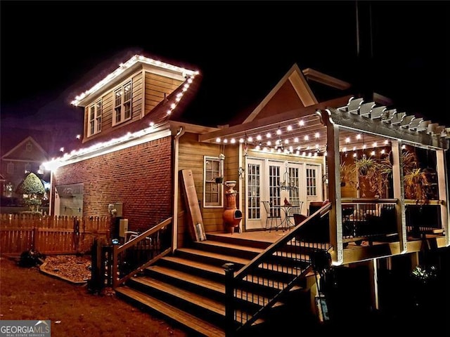 back house at twilight featuring a pergola, french doors, and a deck