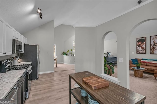 kitchen featuring lofted ceiling, light wood-type flooring, stainless steel appliances, light stone countertops, and white cabinets