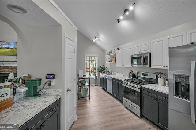 kitchen with white cabinetry, lofted ceiling, stainless steel appliances, light stone countertops, and light hardwood / wood-style flooring