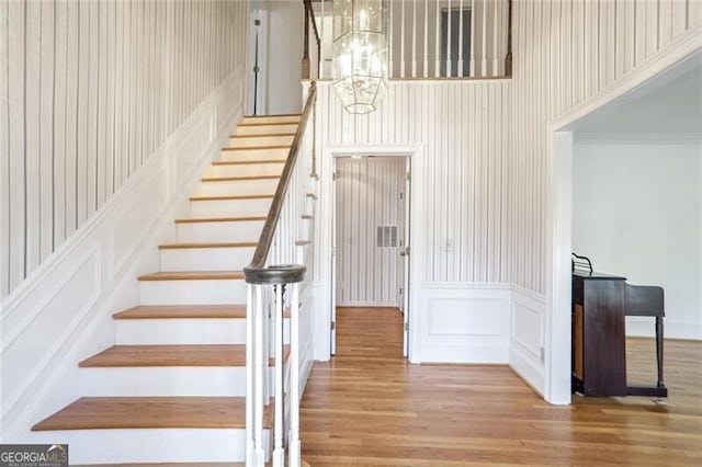 stairway with a notable chandelier, hardwood / wood-style flooring, and ornamental molding