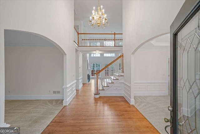 entryway featuring ornamental molding, a towering ceiling, hardwood / wood-style floors, and a notable chandelier