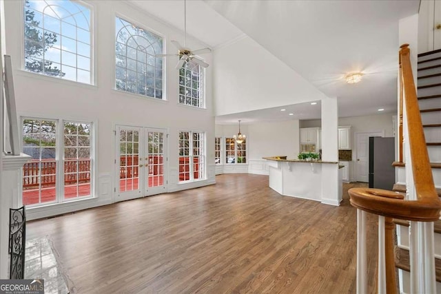 unfurnished living room featuring a high ceiling, wood-type flooring, ceiling fan with notable chandelier, and french doors