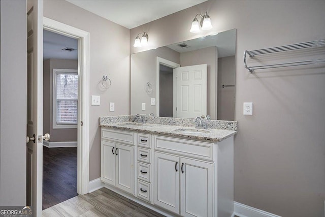 full bath featuring double vanity, wood finished floors, a sink, and baseboards