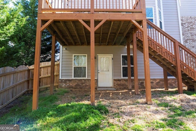 view of exterior entry with a wooden deck, fence, and brick siding