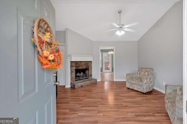 living area with ceiling fan, a fireplace, vaulted ceiling, and light wood-type flooring