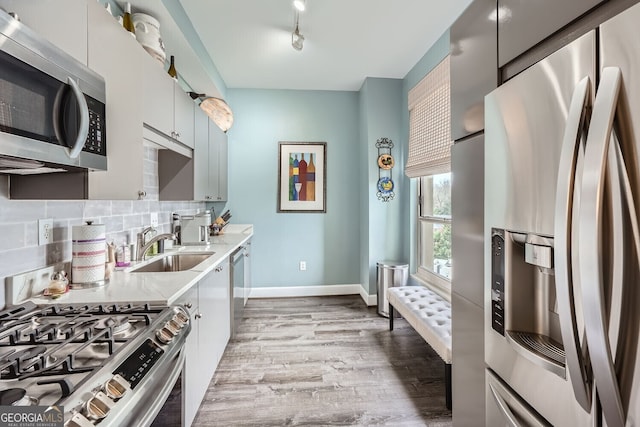 kitchen featuring appliances with stainless steel finishes, tasteful backsplash, rail lighting, sink, and light wood-type flooring