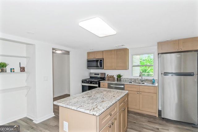 kitchen with a kitchen island, sink, stainless steel appliances, light stone countertops, and light hardwood / wood-style flooring