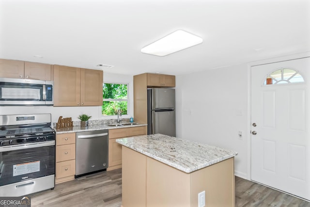 kitchen featuring a kitchen island, appliances with stainless steel finishes, sink, light hardwood / wood-style floors, and light stone countertops