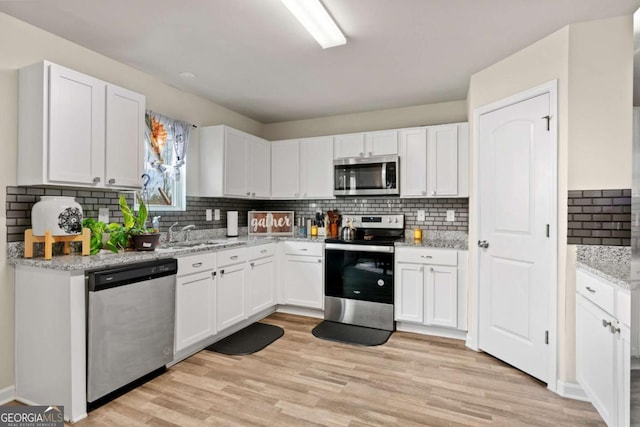 kitchen featuring sink, appliances with stainless steel finishes, white cabinetry, light stone countertops, and light wood-type flooring