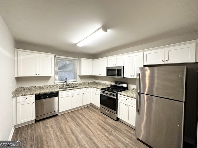 kitchen with sink, light wood-type flooring, stainless steel appliances, light stone countertops, and white cabinets