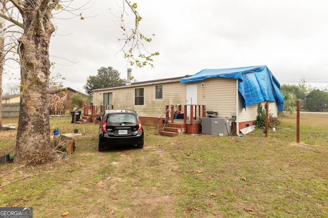 rear view of house with central AC unit and a lawn