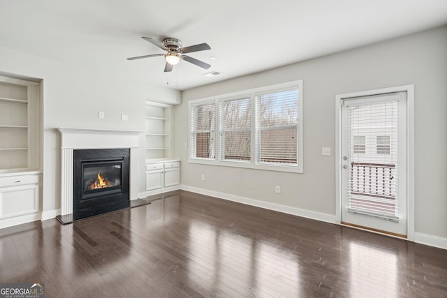 unfurnished living room featuring a fireplace, dark wood-type flooring, built in features, and ceiling fan