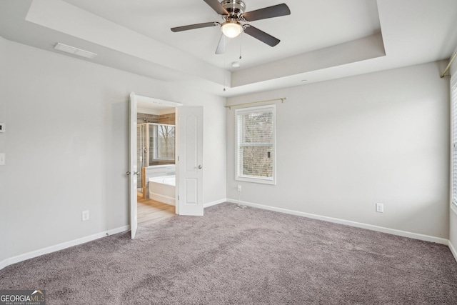 unfurnished bedroom with ceiling fan, ensuite bath, a tray ceiling, and light carpet