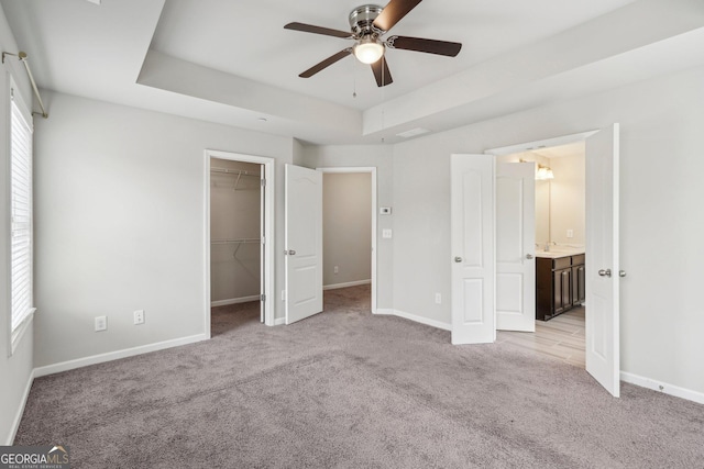 unfurnished bedroom with ceiling fan, a tray ceiling, light carpet, a walk in closet, and a closet