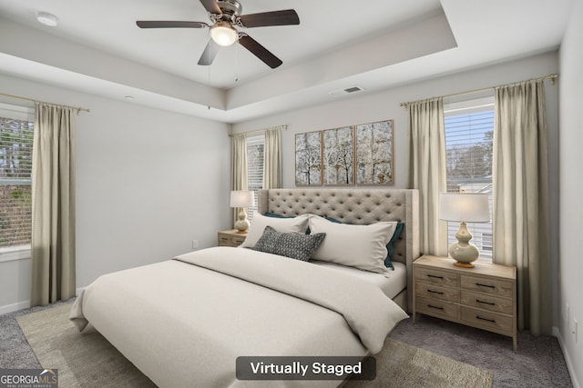 carpeted bedroom with ceiling fan and a tray ceiling