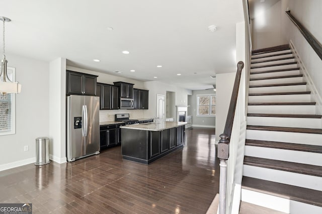 kitchen with pendant lighting, decorative backsplash, light stone counters, stainless steel appliances, and a center island with sink