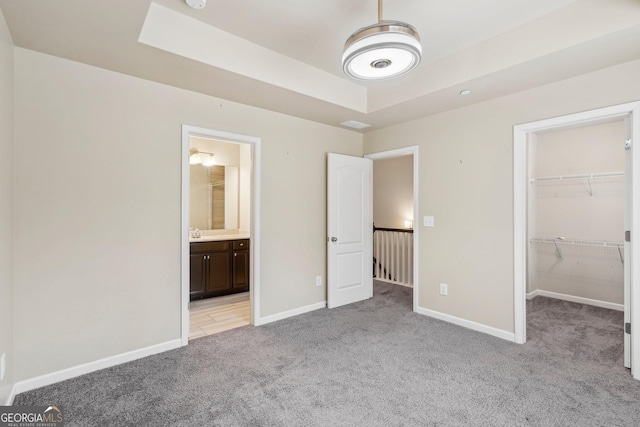 unfurnished bedroom with ensuite bathroom, a raised ceiling, light carpet, a spacious closet, and a closet