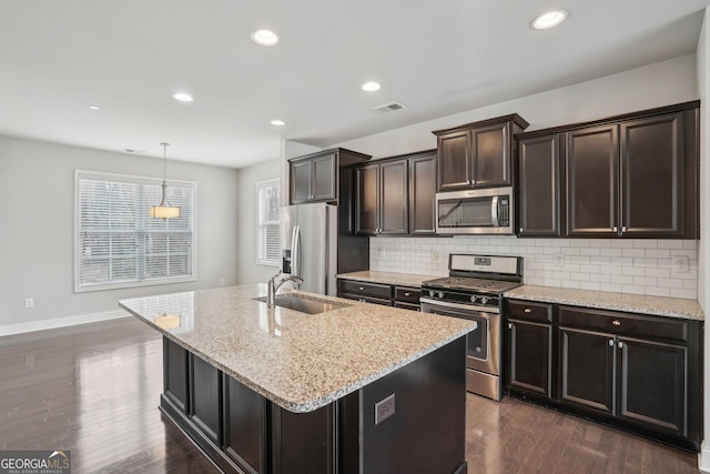 kitchen featuring appliances with stainless steel finishes, sink, hanging light fixtures, dark brown cabinets, and a center island with sink