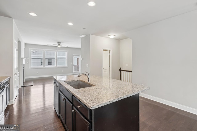 kitchen featuring dark hardwood / wood-style floors, sink, stainless steel dishwasher, light stone countertops, and a center island with sink