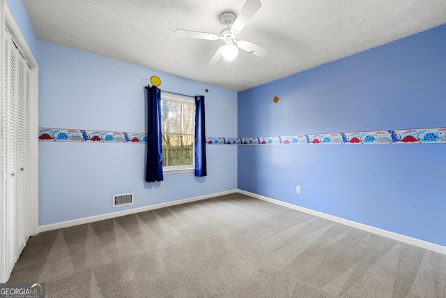 unfurnished bedroom with ceiling fan, carpet, a textured ceiling, and a closet