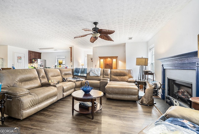 living room with visible vents, dark wood finished floors, a ceiling fan, a textured ceiling, and a fireplace