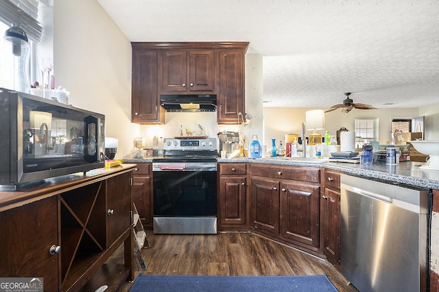 kitchen with a textured ceiling, under cabinet range hood, a sink, appliances with stainless steel finishes, and dark wood-style floors