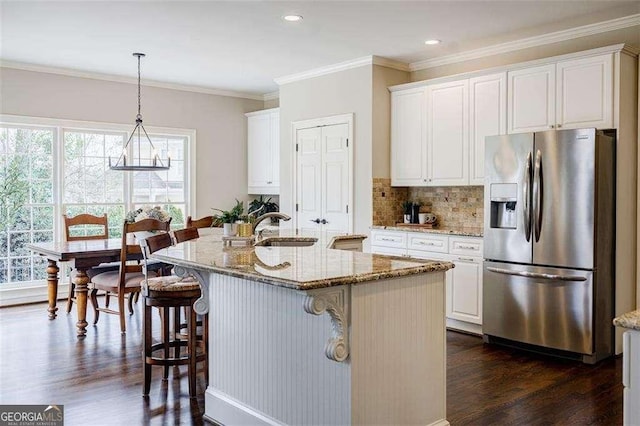 kitchen featuring sink, white cabinetry, stainless steel refrigerator with ice dispenser, light stone counters, and a center island with sink