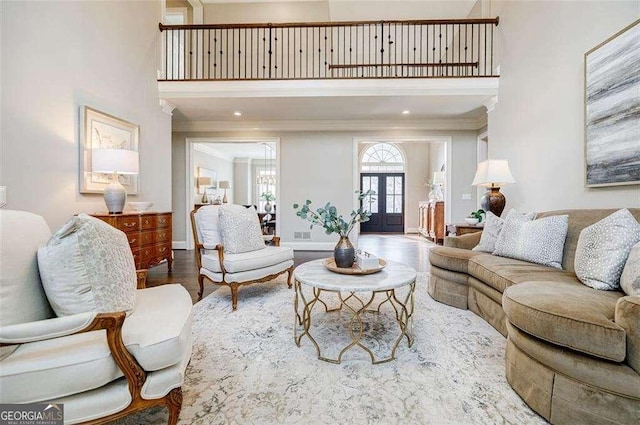 living room with hardwood / wood-style flooring, ornamental molding, a towering ceiling, and french doors