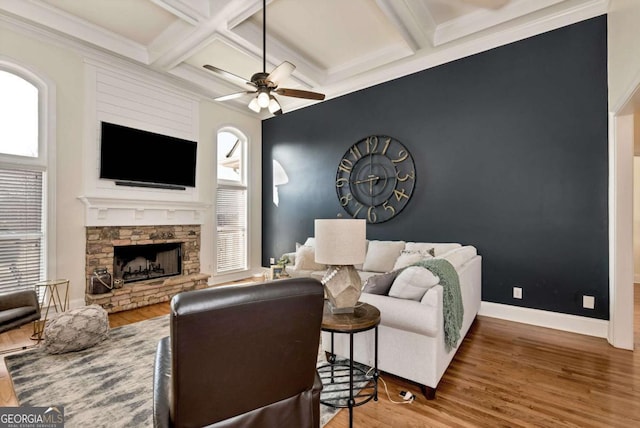 living room featuring hardwood / wood-style flooring, ceiling fan, beam ceiling, coffered ceiling, and a stone fireplace