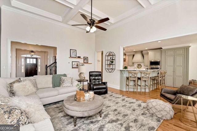 living room with coffered ceiling, crown molding, beam ceiling, light hardwood / wood-style floors, and a high ceiling