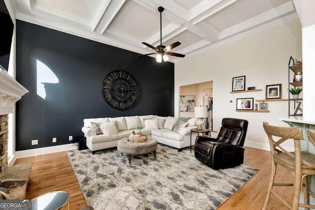 living room with ceiling fan, a stone fireplace, coffered ceiling, and light wood-type flooring