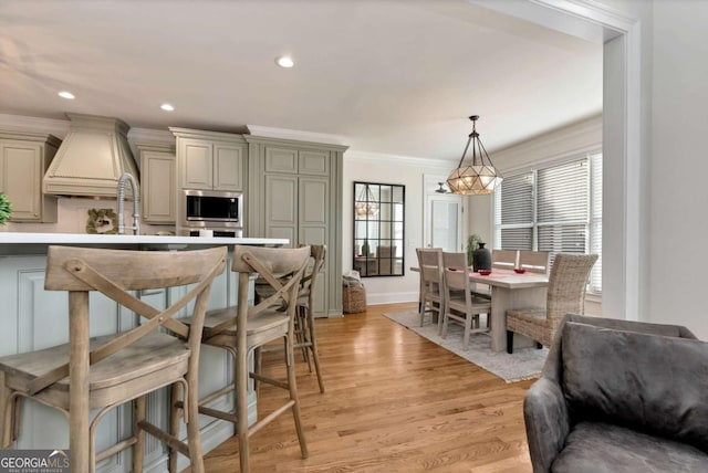 kitchen with crown molding, hanging light fixtures, light wood-type flooring, stainless steel microwave, and cream cabinets