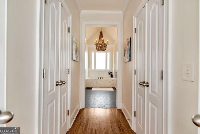 corridor with crown molding, wood-type flooring, and a chandelier