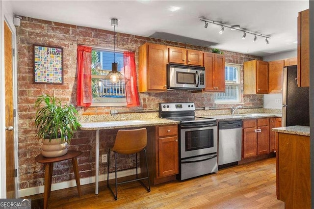 kitchen with a breakfast bar area, hanging light fixtures, stainless steel appliances, light stone countertops, and light hardwood / wood-style floors