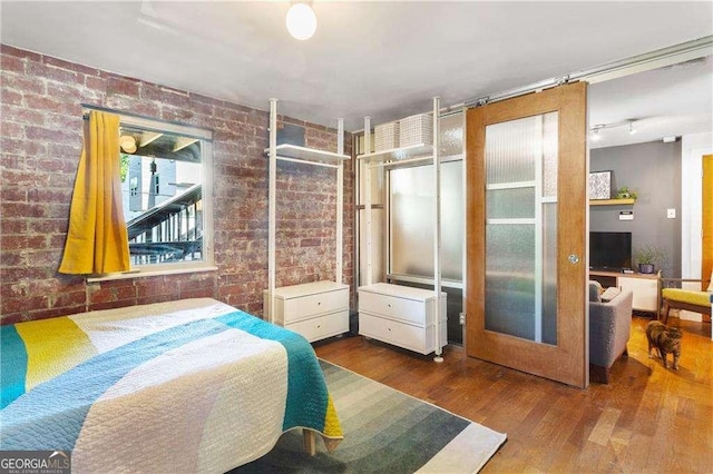 bedroom featuring brick wall and dark hardwood / wood-style flooring