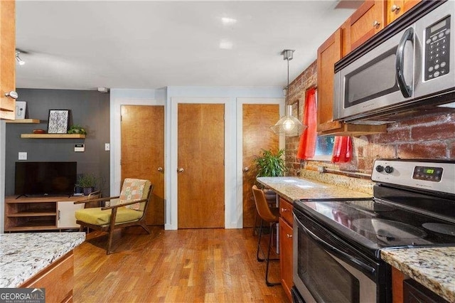 kitchen with built in desk, light hardwood / wood-style flooring, appliances with stainless steel finishes, pendant lighting, and light stone countertops