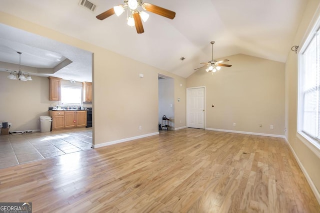 unfurnished living room featuring ceiling fan with notable chandelier, vaulted ceiling, a raised ceiling, and light wood-type flooring