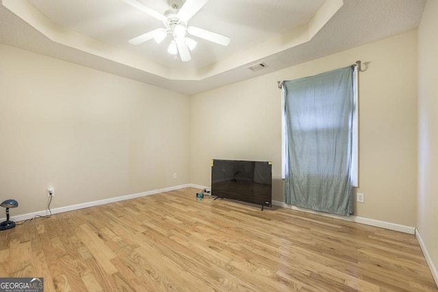 spare room featuring ceiling fan, light wood-type flooring, and a tray ceiling