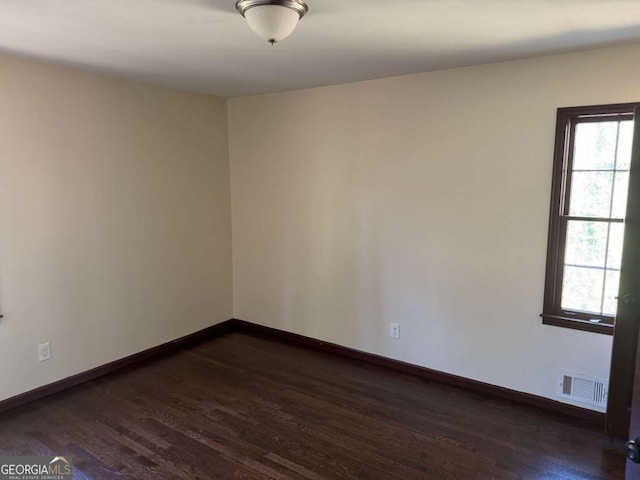 empty room with a wealth of natural light and dark hardwood / wood-style flooring