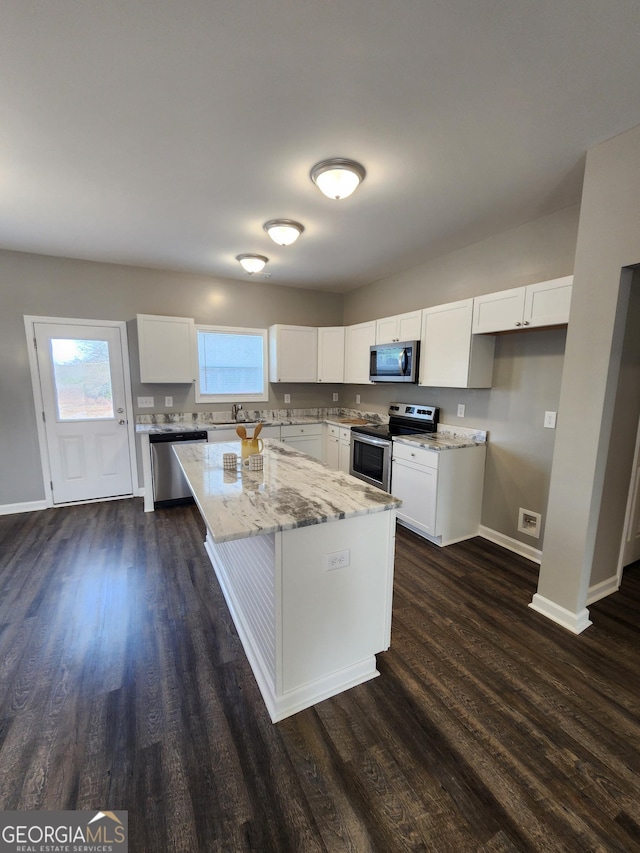 kitchen featuring white cabinetry, dark hardwood / wood-style flooring, a kitchen island, stainless steel appliances, and light stone countertops