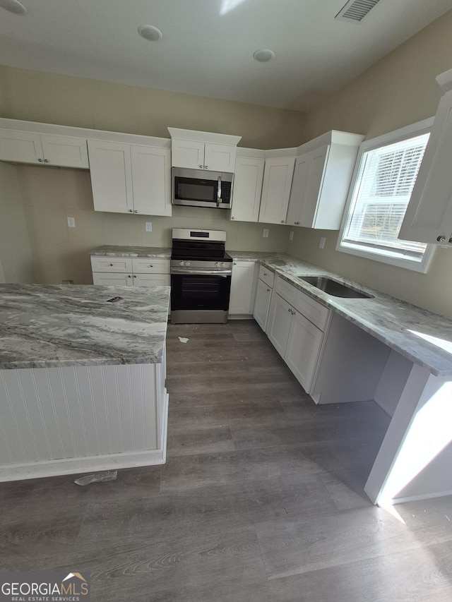 kitchen with white cabinets, light stone countertops, dark wood-style flooring, and stainless steel appliances