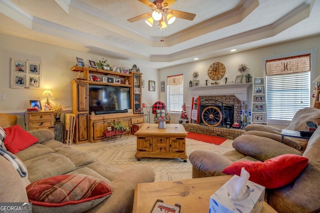 living room featuring ornamental molding, a healthy amount of sunlight, a raised ceiling, and a brick fireplace