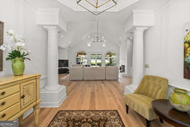 foyer entrance featuring crown molding, light hardwood / wood-style flooring, an inviting chandelier, high vaulted ceiling, and ornate columns