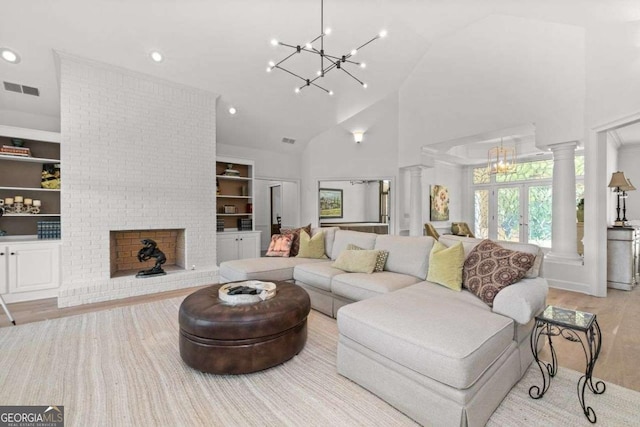 living room featuring ornate columns, a notable chandelier, built in features, and light hardwood / wood-style flooring