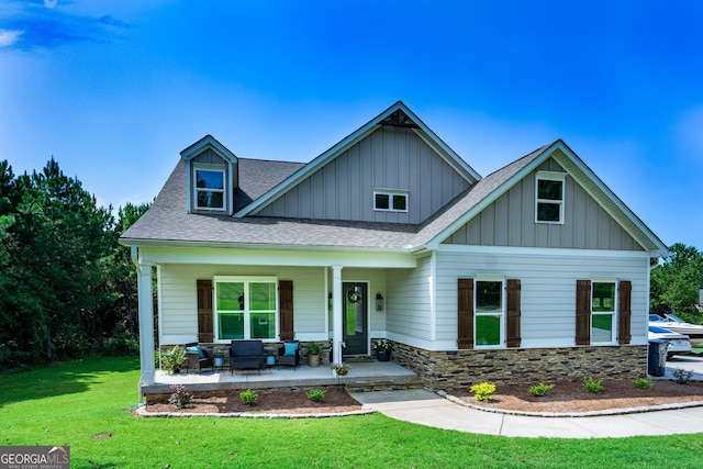 view of front of house with covered porch, a shingled roof, stone siding, board and batten siding, and a front yard