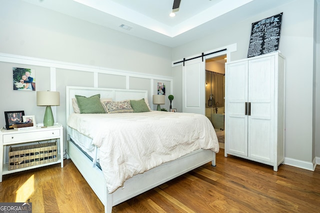 bedroom with dark wood-style floors, a barn door, visible vents, and a ceiling fan