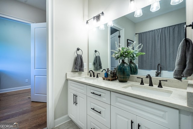 full bath featuring double vanity, baseboards, a sink, and wood finished floors