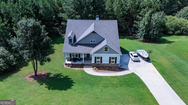 view of front of house featuring driveway, stone siding, covered porch, a front lawn, and board and batten siding