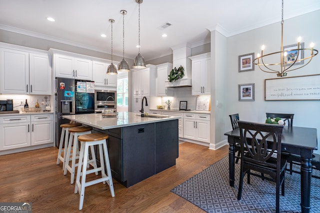 kitchen featuring stainless steel appliances, white cabinets, a center island with sink, and hanging light fixtures