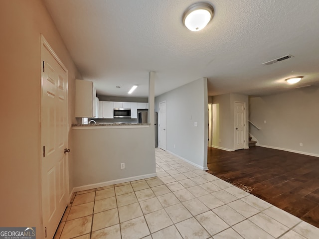 kitchen with white cabinetry, a textured ceiling, light wood-type flooring, appliances with stainless steel finishes, and kitchen peninsula